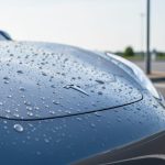 Close-up of an electric vehicle’s hood with water droplets beading on a glossy ceramic-coated paint surface.